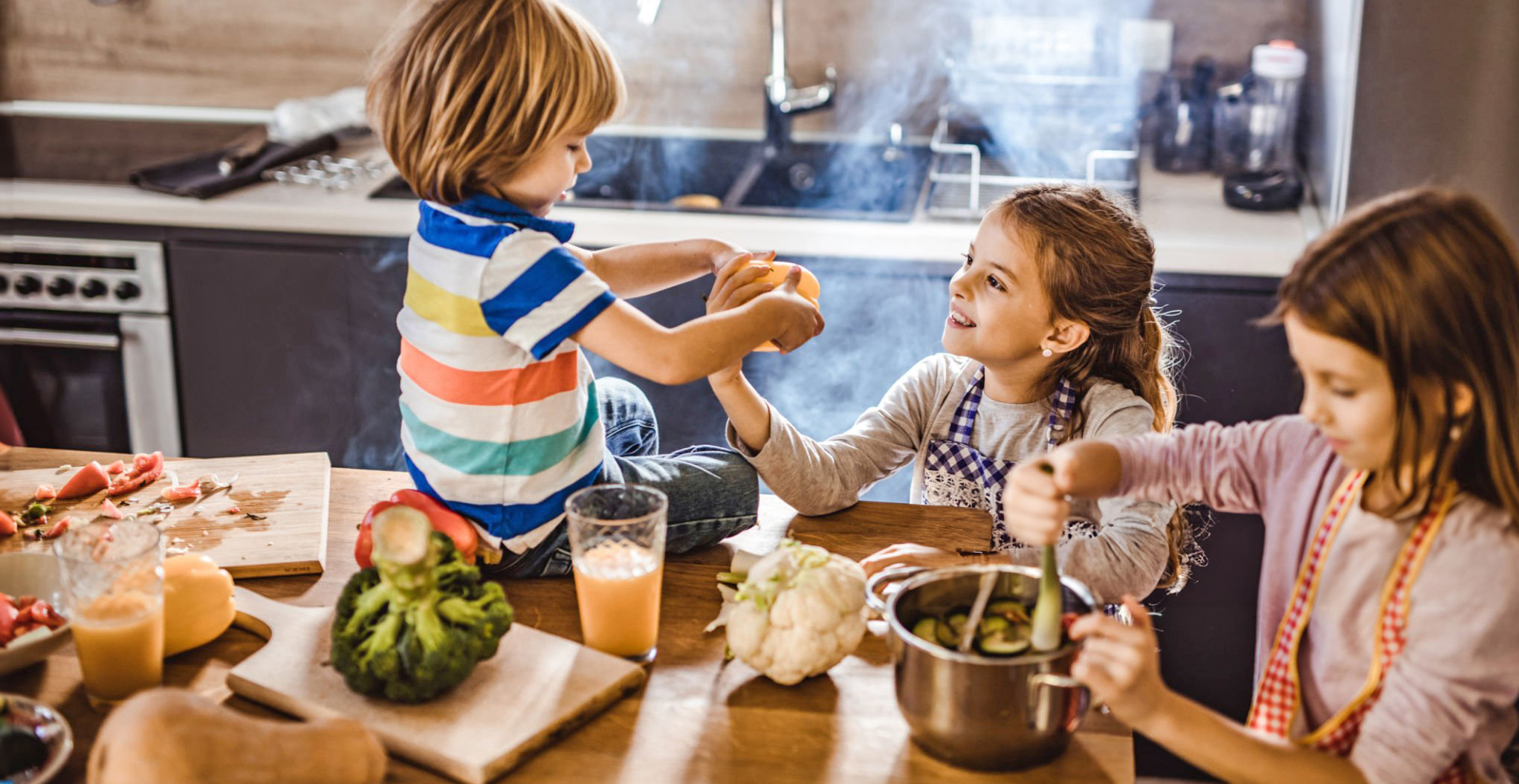 Kinder kochen zusammen in Küche, schneiden Gemüse und rühren im Topf