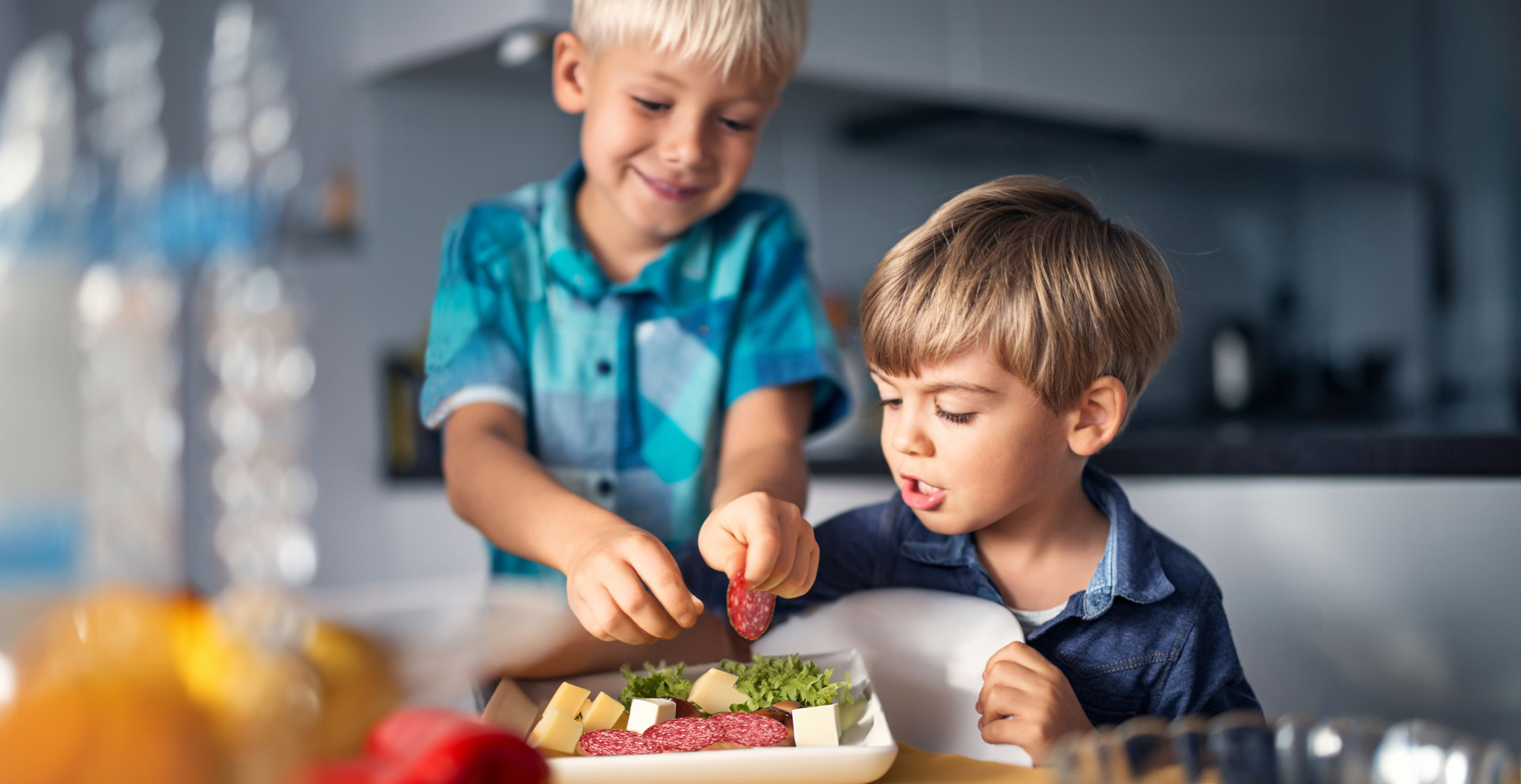 Zwei Kinder belegen Teller mit Käse, Gemüse und Wurst in der Küche
